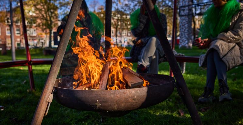 Drie mensen zitten in een park rond een vuurkorf