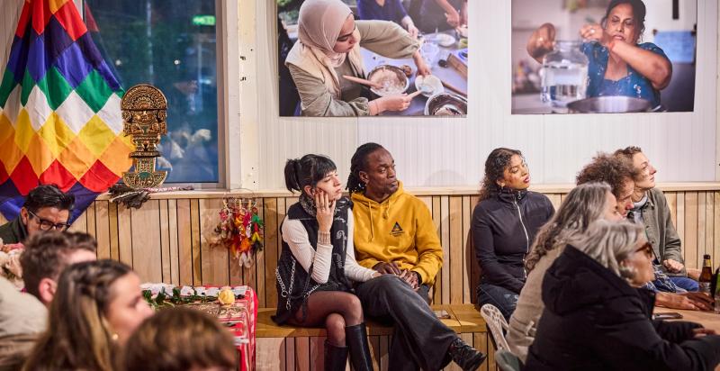 Groepje mensen zit in de tentoonstellingsruimte in De HER te luisteren naar een spreker op het podium.