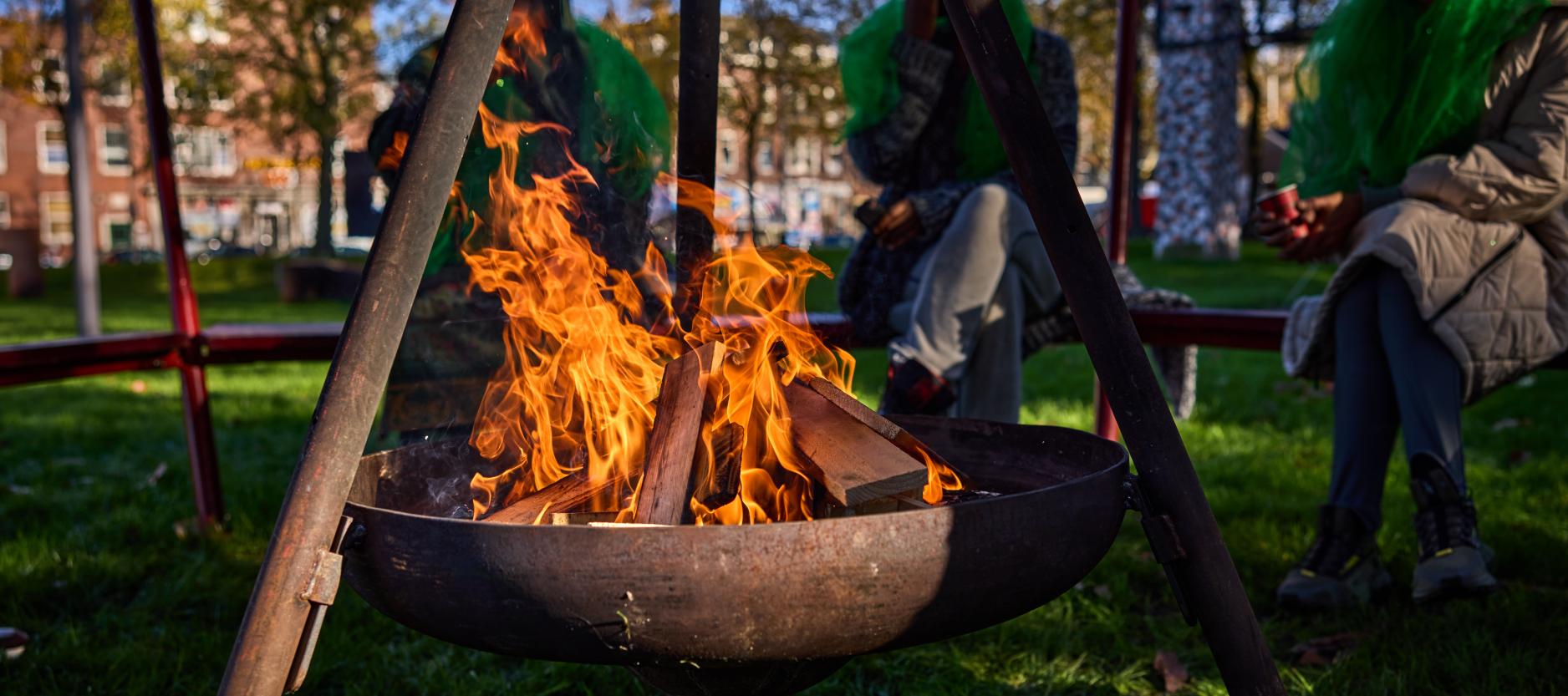 Drie mensen zitten in een park rond een vuurkorf