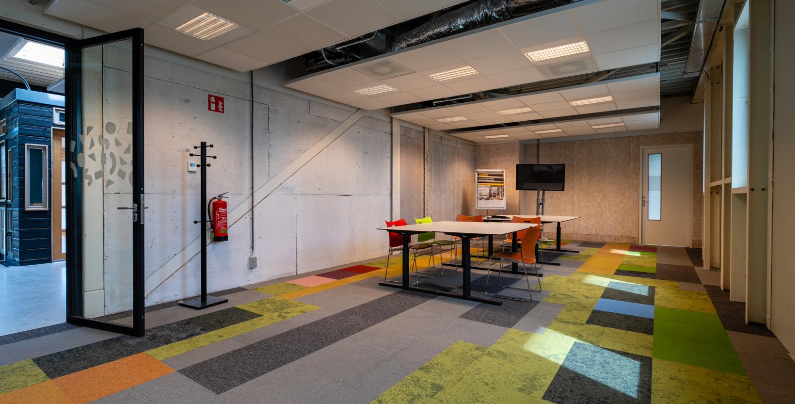 Grote vergaderruimte in circulair Centrum De HER. Op de vloer liggen allerlei kleuren tapijtegels.