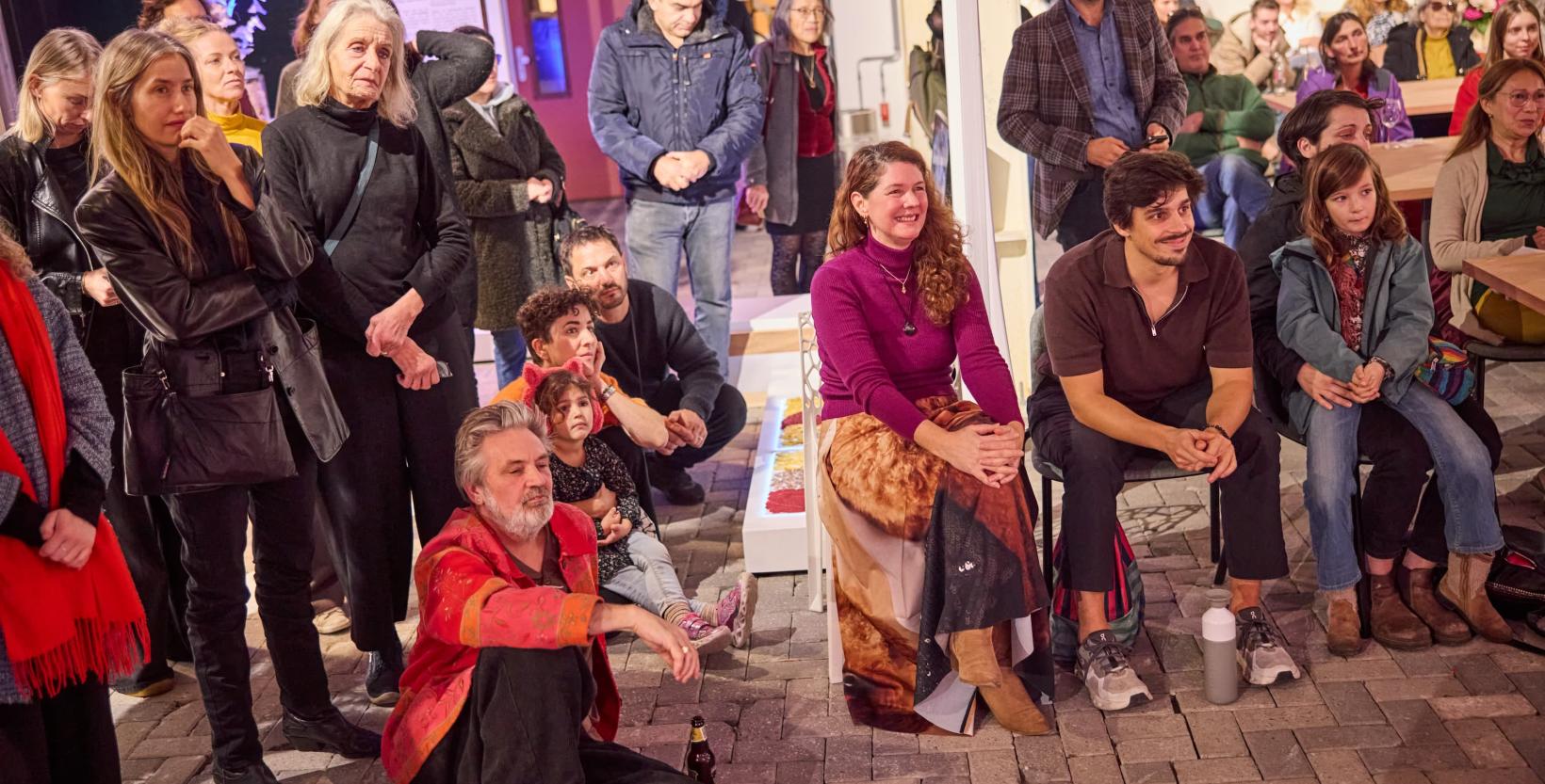 Groep mensen zit en staat lachend te luisteren naar een spreker bij circulair centrum De HER.